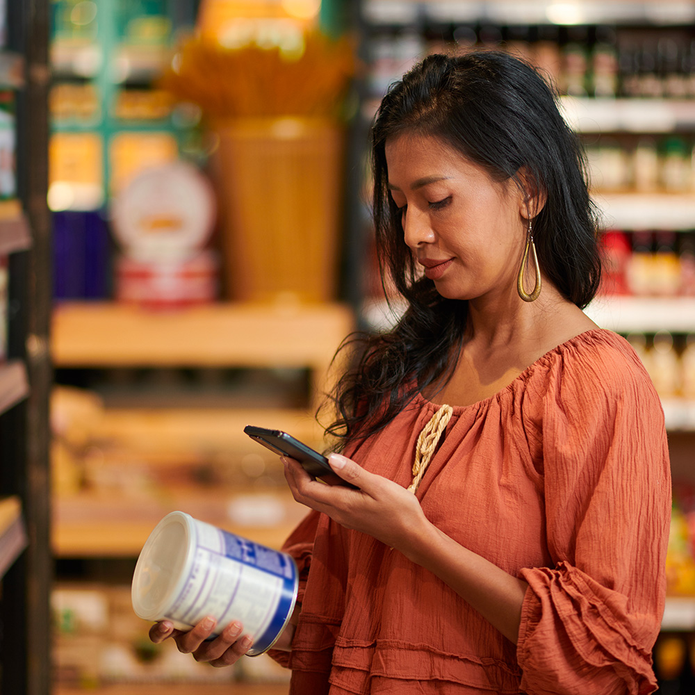 Woman checking her phone while holding a grocery item.